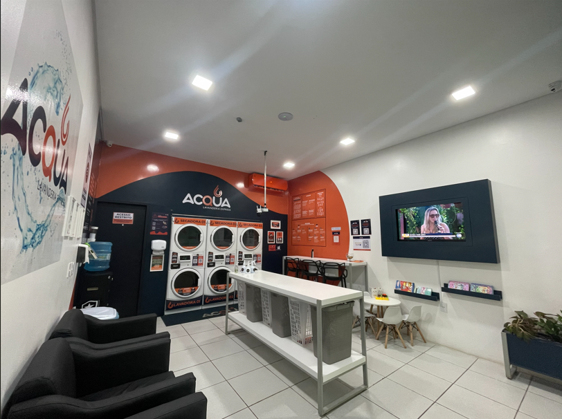 Interior da lavanderia de autoatendimento Acqua em Parnaíba, com TV e espaço de espera